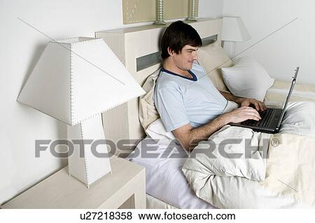 Young man in bed with laptop computer View Large Photo Image Stock Photo - Young man in bed with laptop computer. Fotosearch