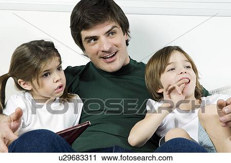 Stock Image - Young man on couch with children and a book. Fotosearch