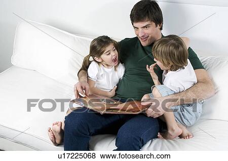 Stock Photo - Young man on couch with children reading. Fotosearch