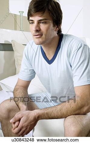 Young man sitting on bed View Large Photo Image Stock Photo - Young man sitting on bed. Fotosearch