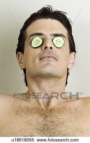 Stock Photography - Young man with cucumber slices on his eyes. Fotosearch