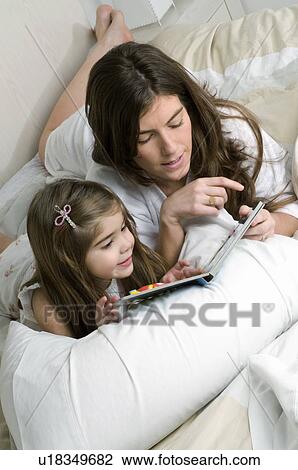 Young woman and girl on bed reading a book View Large Photo Image Stock Image - Young woman and girl on bed reading a book. Fotosearch