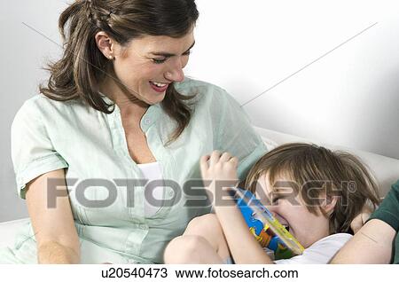 Stock Image - Young woman on couch with boy reading. Fotosearch