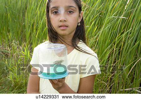 Stock Image - 8 year old girl in wetland holding frog in collecting jar, Winnipeg, Canada. Fotosearch