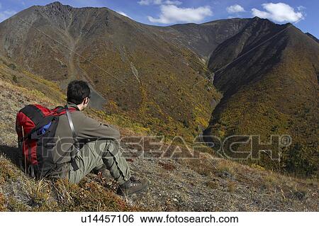 Stock Photograph - A lone hiker pauses to admire the centre ridge of Caribou Mountain - located outside Whitehorse, Yukon near the small native village of Carcross - which is coloured with vibrant autum hues.. Fotosearch