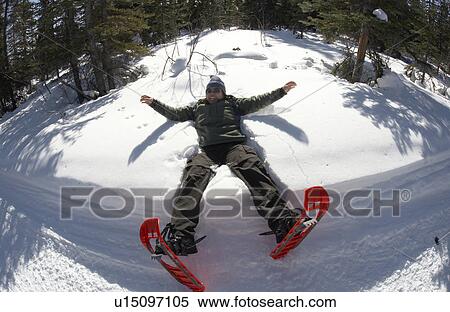 Stock Photography - A snowshoer falls backwards into the snow to make a late winter snow angel, only to remember after-the-fact that she forgot to wear her gloves. Coal Lake Trail outside Whitehorse, Yukon.. Fotosearch