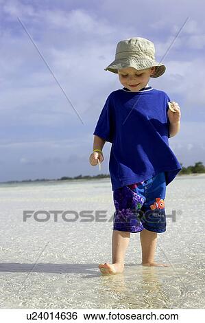 Stock Photograph - Boy standing in shallow water on beach, CamagÃƒÂ¼ey, Cuba. Fotosearch