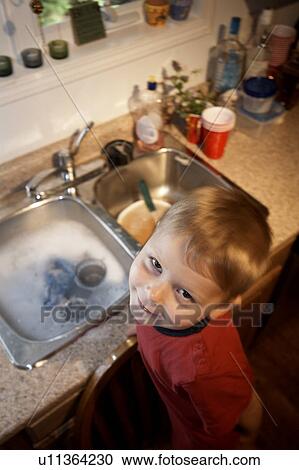 Boy standing on chair at kitchen sink washing dishes View Large Photo Image Stock Image - Boy standing on chair at kitchen sink washing dishes. Fotosearch