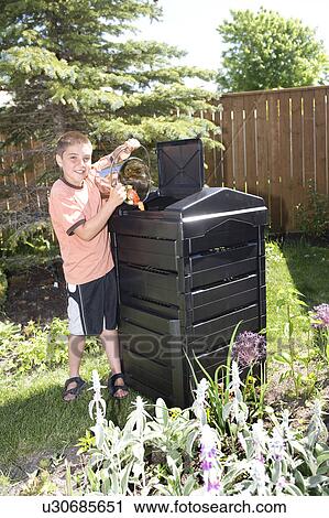 Stock Image - Boy with compost pail beside composter in backyard, Winnipeg, Canada. Fotosearch
