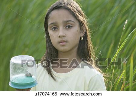 Stock Photography - Eight year old girl holding frog in collecting jar in wetland, Winnipeg, Canada. Fotosearch