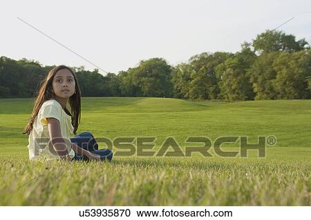 Stock Image - Eight year old girl seated on grass in park, Winnipeg, Canada. Fotosearch