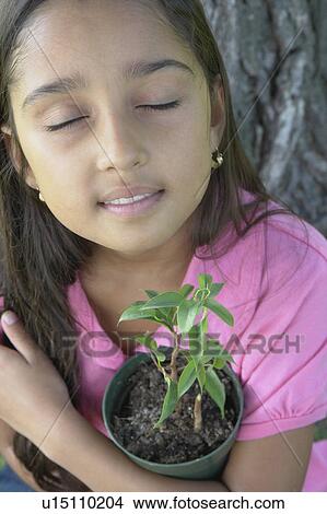 Picture - Eight year old girl with closed eyes holding small tree beside large tree, Winnipeg, Canada. Fotosearch