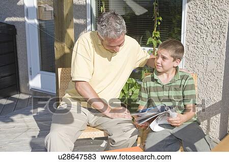 Father and son looking at magazine, seated on deck, Winnipeg, Canada View Large Photo Image Stock Image - Father and son looking at magazine, seated on deck, Winnipeg, Canada. Fotosearch
