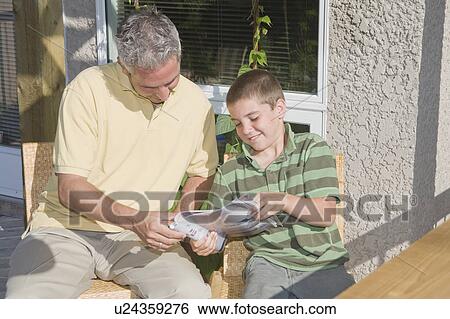 Father and son looking at magazine, seated on deck, Winnipeg, Canada View Large Photo Image Stock Photograph - Father and son looking at magazine, seated on deck, Winnipeg, Canada. Fotosearch