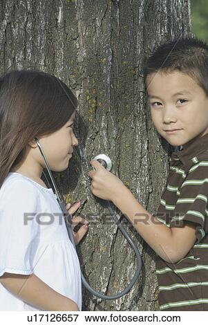 Stock Photo - Five year old sister and seven year old brother with stethescope on tree, Winnipeg, Canada. Fotosearch