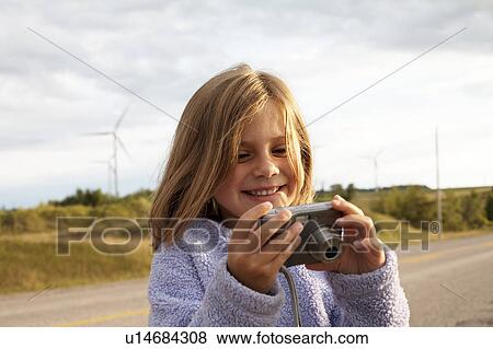 Stock Photo - Girl looking at digital camera in front of wind turbines, Tiverton, Bruce Peninsula, Ontario. Fotosearch