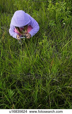 Girl looking at digital camera while stooping in grassy field View Large Photo Image Picture - Girl looking at digital camera while stooping in grassy field. Fotosearch