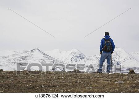 Picture - Hiker overlooks snow-covered mountains outside of Whitehorse, Yukon, along the Fish Lake hiking trail.. Fotosearch