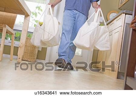 Stock Image - Lower half of man carrying groceries in cloth grocery bags, Winnipeg, Canada. Fotosearch