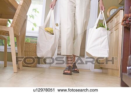 Stock Image - Lower half of woman carrying groceries in cloth grocery bags, Winnipeg, Canada. Fotosearch