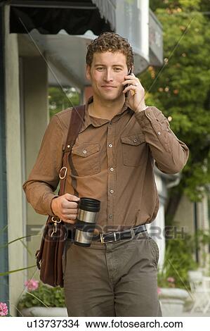 Picture - Man with coffee thermos and cellphone on urban street, Winnipeg, Canada. Fotosearch