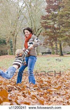 Stock Image - Mom swings son around in autumn leaves, Vancouver, British Columbia. Fotosearch