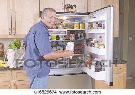 Picture - Senior man unloads cloth grocery bags into refridgerator, Winnipeg, Canada. Fotosearch