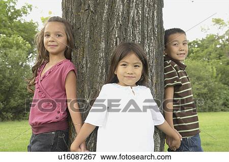Stock Photo - Seven and five year old girls and seven year old boy hold hands around tree, Winnipeg, Canada. Fotosearch
