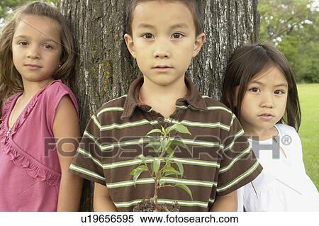Stock Photography - Seven and five year old girls and seven year old boy holding small tree, Winnipeg, Canada. Fotosearch