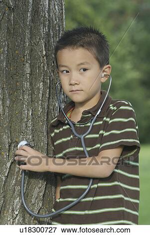Stock Photo - Seven year old boy with stethescope placed on tree, Winnipeg, Canada. Fotosearch