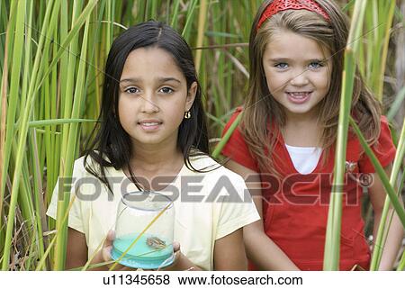 Stock Photo - Six year old and 8 year old girls in wetland holding frog in collecting jar, Winnipeg, Canada. Fotosearch
