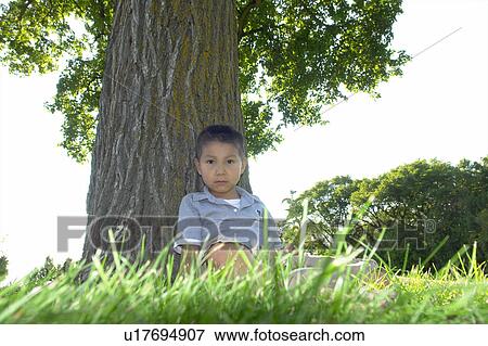 Stock Photo - Six year old boy seated beside large tree, Winnipeg, Canada. Fotosearch