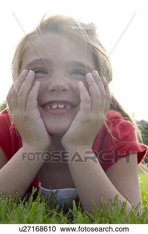 Stock Image - Six year old girl with chin in hands lying on grass, Winnipeg, Canada. Fotosearch