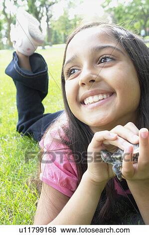 Stock Photo - Smiling eight year old girl lying in grass with turtle, Winnipeg, Canada. Fotosearch