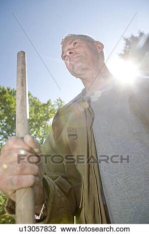 Stock Image - Sunflare, senior man holding hoe, Winnipeg, Canada. Fotosearch