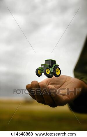 Stock Photo - Tiny tractor floats above farmer's hand, Lumsden, Saskatchewan. Fotosearch
