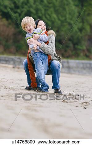 Stock Photo - Woman and boy laughing in embrace on beach, Vancouver, British Columbia. Fotosearch
