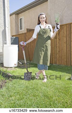 Stock Photo - Woman holding tree seedling in front of rain barrel, Winnipeg, Canada. Fotosearch