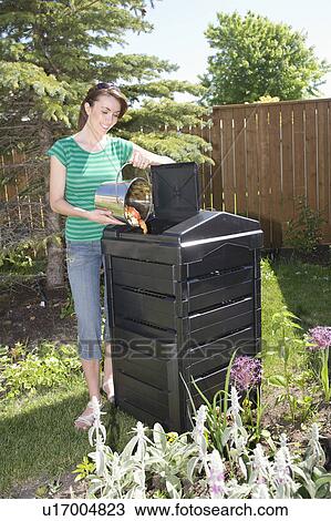 Stock Image - Woman with compost pail beside composter in backyard, Winnipeg, Canada. Fotosearch