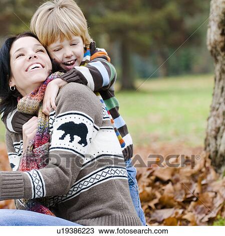 Stock Image - Young boy embraces mother from behind, outdoor in autumn, Vancouver, British Columbia. Fotosearch