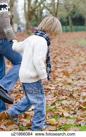 Picture - Young boy walking through autumn leaves holding woman's hand, Vancouver, British Columbia. Fotosearch