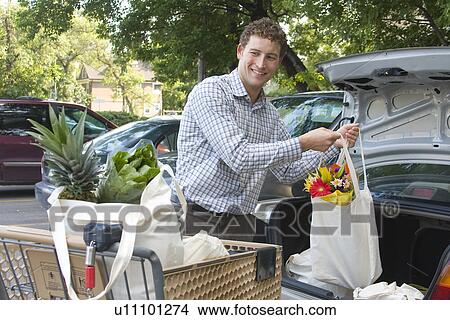 Picture - Young man loading groceries in cloth bags, into car, Winnipeg, Canada. Fotosearch