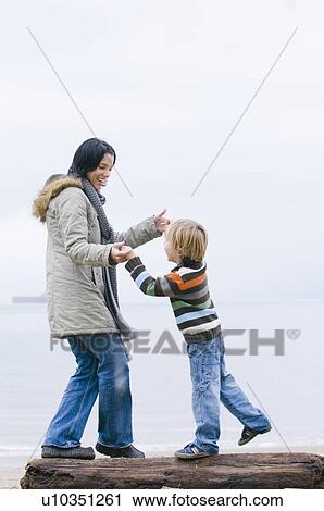 Stock Image - Young woman and boy balancing on log on beach, Vancouver, British Columbia. Fotosearch