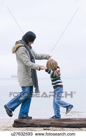 Stock Image - Young woman and boy balancing on log on beach, Vancouver, British Columbia. Fotosearch