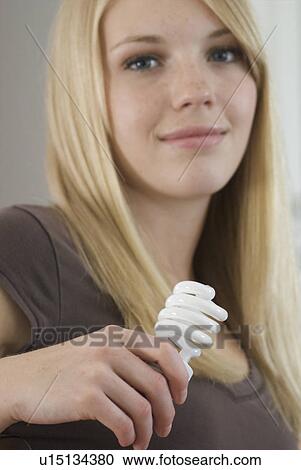 Stock Image - Young woman holding compact fluorescent bulb in kitchen, Brandon, Canada. Fotosearch