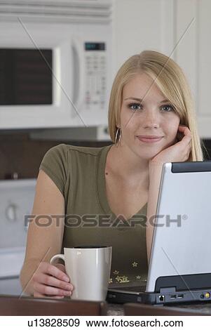 Stock Photo - Young woman in front of laptop computer in kitchen, Brandon, Canada. Fotosearch