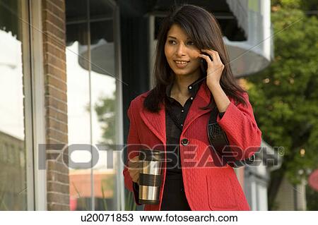 Stock Image - Young woman with coffee thermos and cellphone on urban street, Winnipeg, Canada. Fotosearch