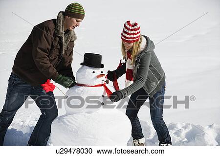 Stock Image - A couple making a snowman. Fotosearch