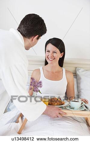 Stock Image - A man bringing a woman breakfast in bed. Fotosearch