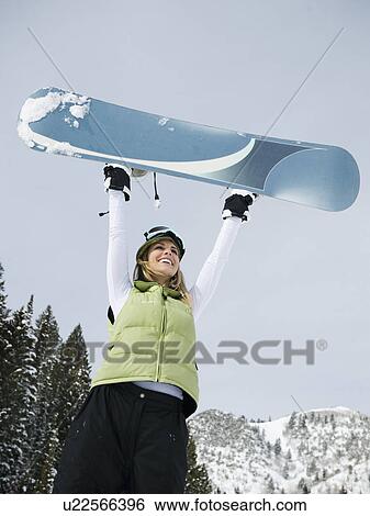 A snowboarder holding up her snowboard View Large Photo Image Stock Photograph - A snowboarder holding up her snowboard. Fotosearch